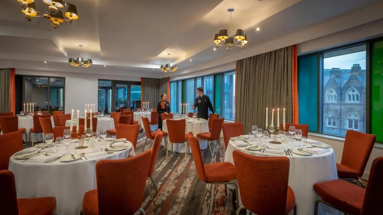 a banquet room with tables and chairs and a woman at Clayton Hotel Cardiff in Cardiff